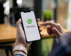 Image of a person holding a phone with the WhatsApp icon on the screen.