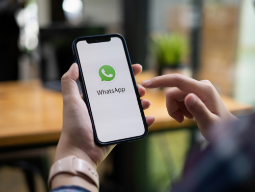 Image of a person holding a phone with the WhatsApp icon on the screen.