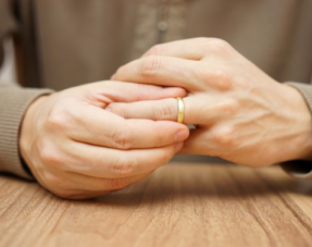 Image of a person with a wedding ring on and their hands together on a table.