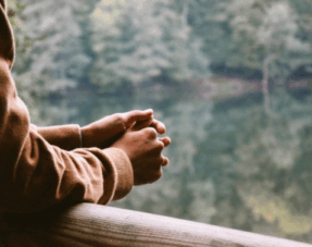 Image of a woman standing outside with her arms resting on a balcony with trees in the distance, illustrating the possible impact of co-parenting on mental health.