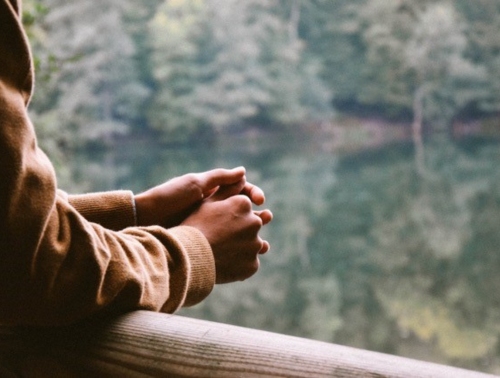 Image of a woman standing outside with her arms resting on a balcony with trees in the distance, illustrating the possible impact of co-parenting on mental health.