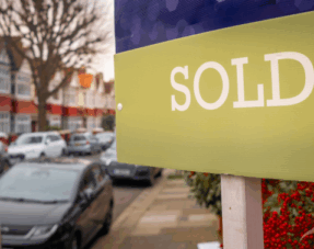 Image of a "sold" sign in front of a house on a residential street.