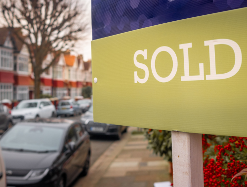 Image of a "sold" sign in front of a house on a residential street.