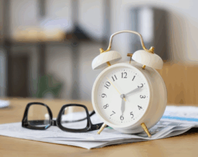 A classic alarm clock and reading glasses resting on documents, symbolising time sensitivity.