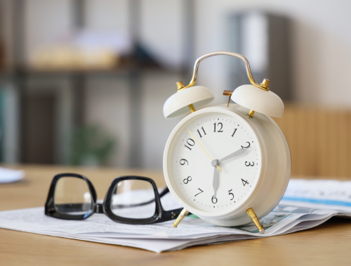 A classic alarm clock and reading glasses resting on documents, symbolising time sensitivity.