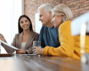 A young professional woman discusses documents with an older couple at a meeting.
