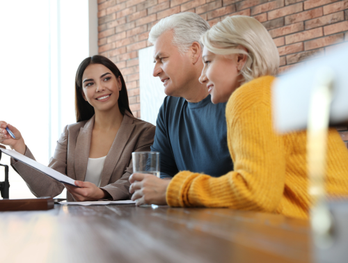 A young professional woman discusses documents with an older couple at a meeting.