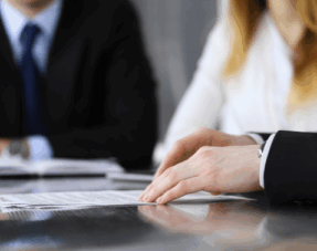 Three people sitting at a table, reviewing a document, representing Alternative Dispute Resolution (ADR) methods.