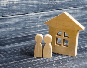 Wooden figures standing next to a wooden house, symbolising cohabitating couples.