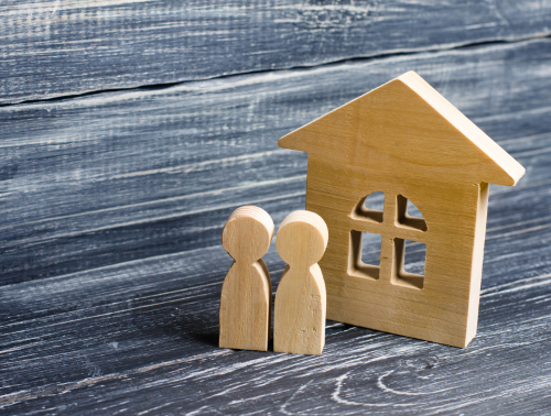 Wooden figures standing next to a wooden house, symbolising cohabitating couples.