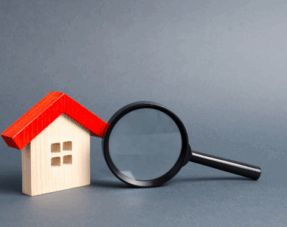 Image of a wooden house and magnifying glass on a grey background, representing property searches.