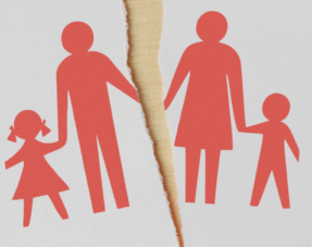 Silhouette of a family holding hands on a piece of paper torn in half down the middle, implying family disputes.