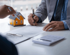 Close-up of people signing property documents with a model house on the table.