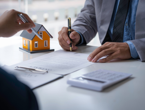 Close-up of people signing property documents with a model house on the table.